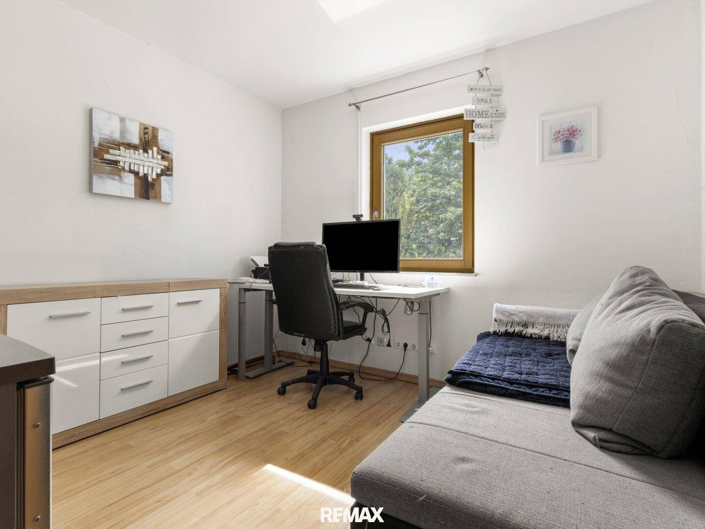 Helles Arbeitszimmer mit Holzboden, Schreibtisch und Blick ins Grüne durch das Fenster.