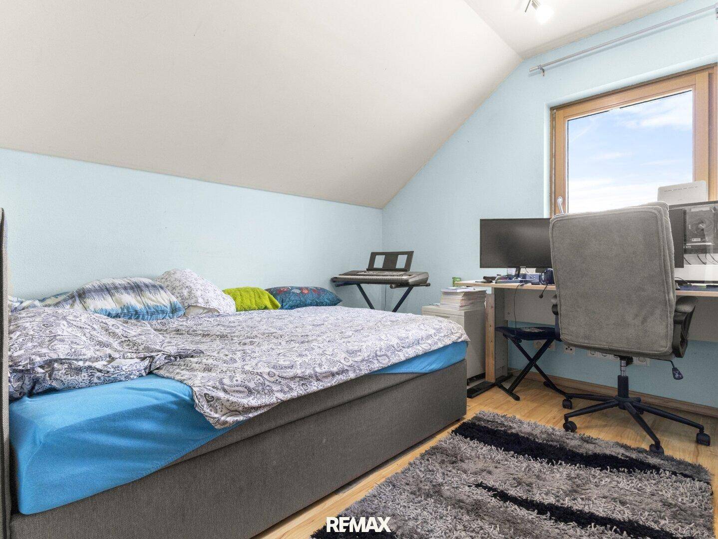 Helles Schlafzimmer mit Dachschräge, Einzelbett und Arbeitsbereich am Fenster.