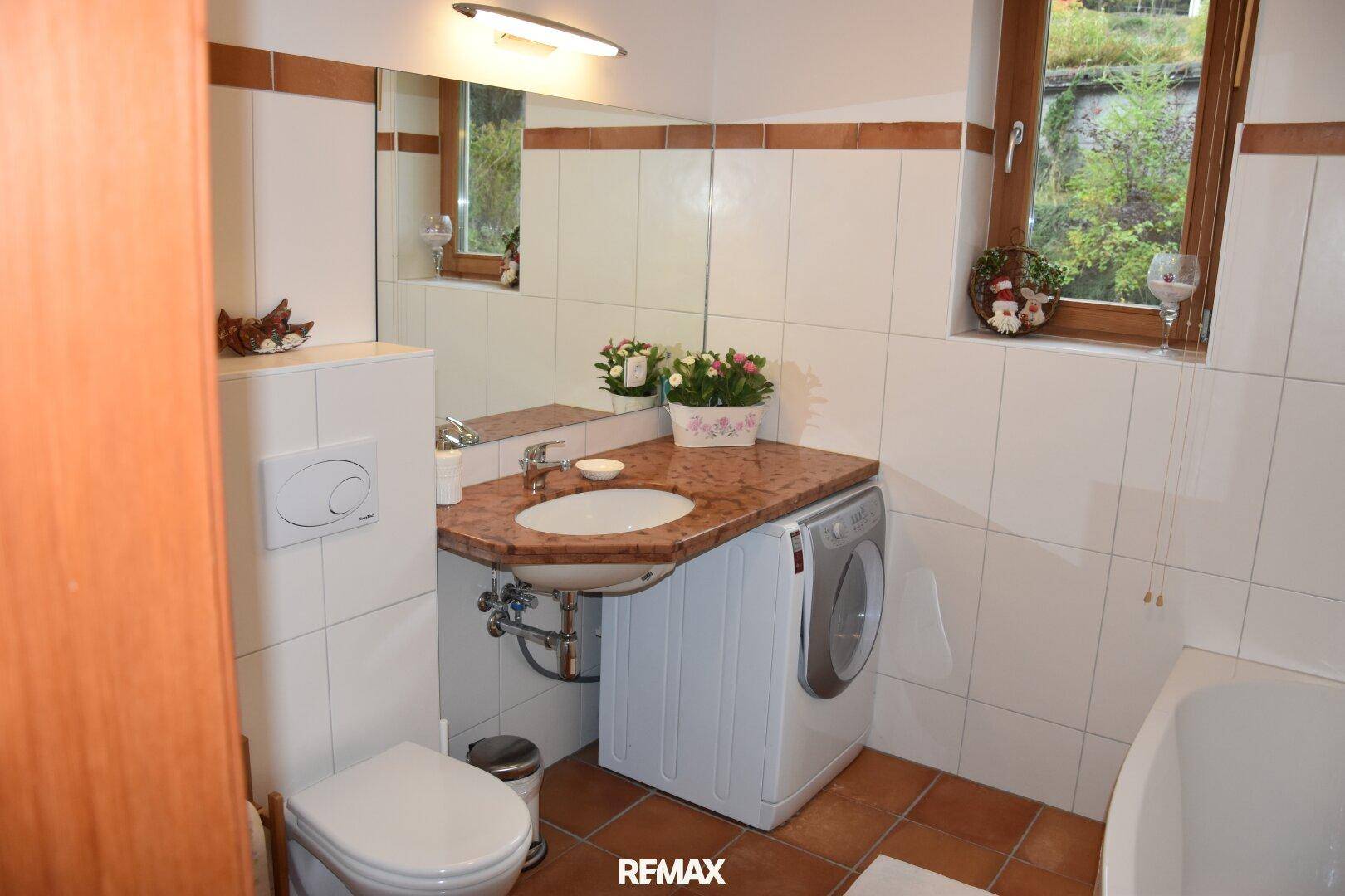 Badezimmer mit Waschbecken, Toilette, Badewanne und integrierter Waschmaschine, hell gefliest.
