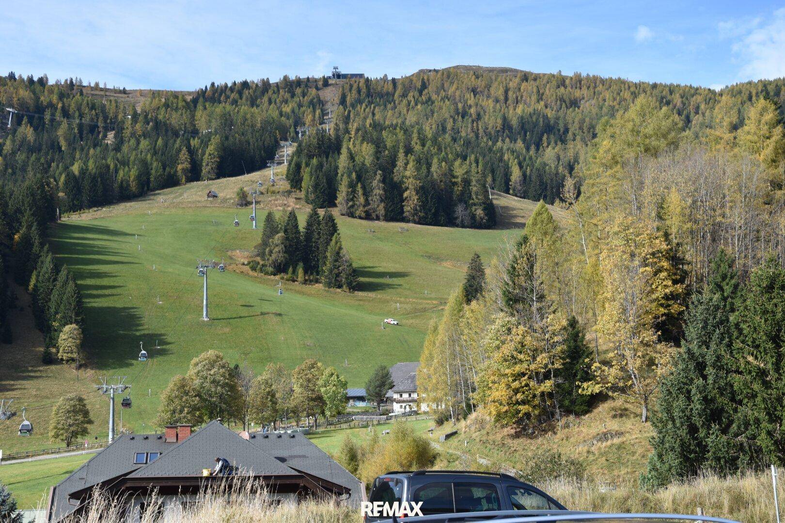Weitläufige Skipiste mit Liftanlagen und bewaldeten Bergen unter strahlend blauem Himmel.