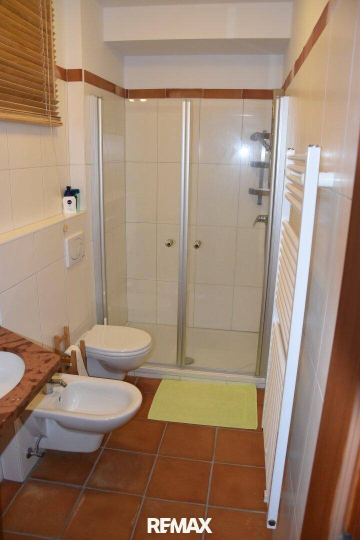 Badezimmer mit Dusche, Bidet, Toilette und beheiztem Handtuchhalter, in warmen Farbtönen gefliest.