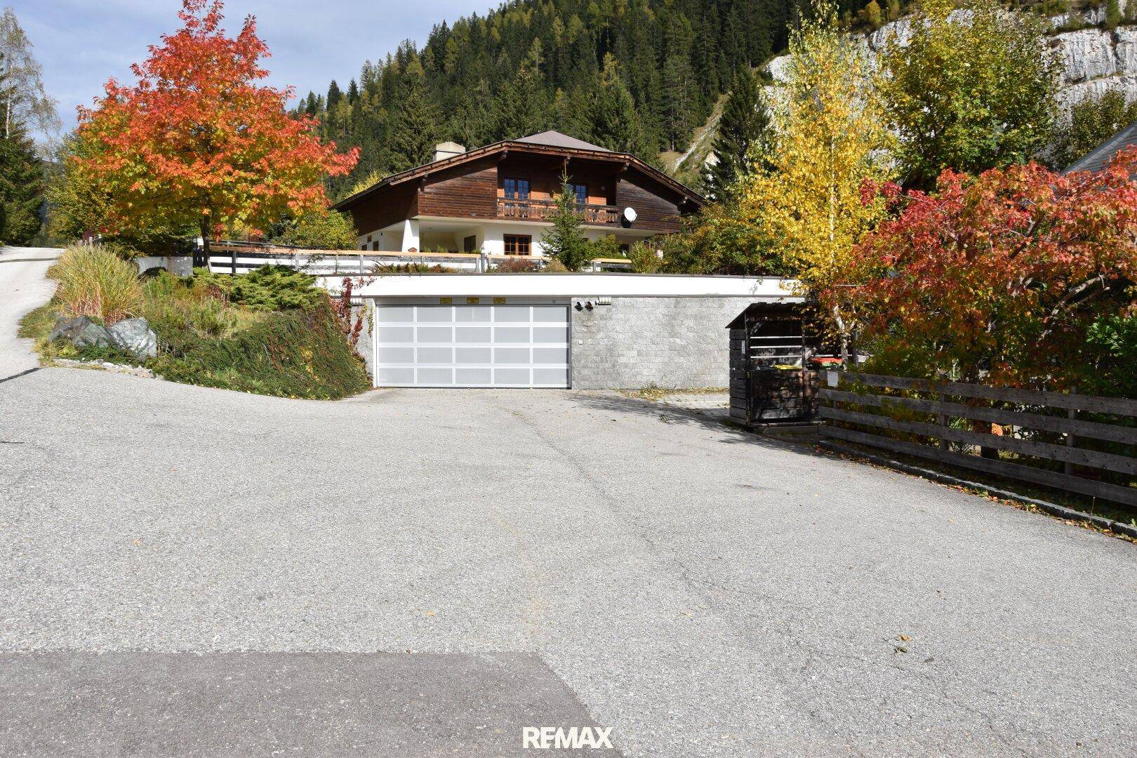 Zufahrt zur Tiefgarage mit einem Garagentor und umgebender Natur im Herbst.