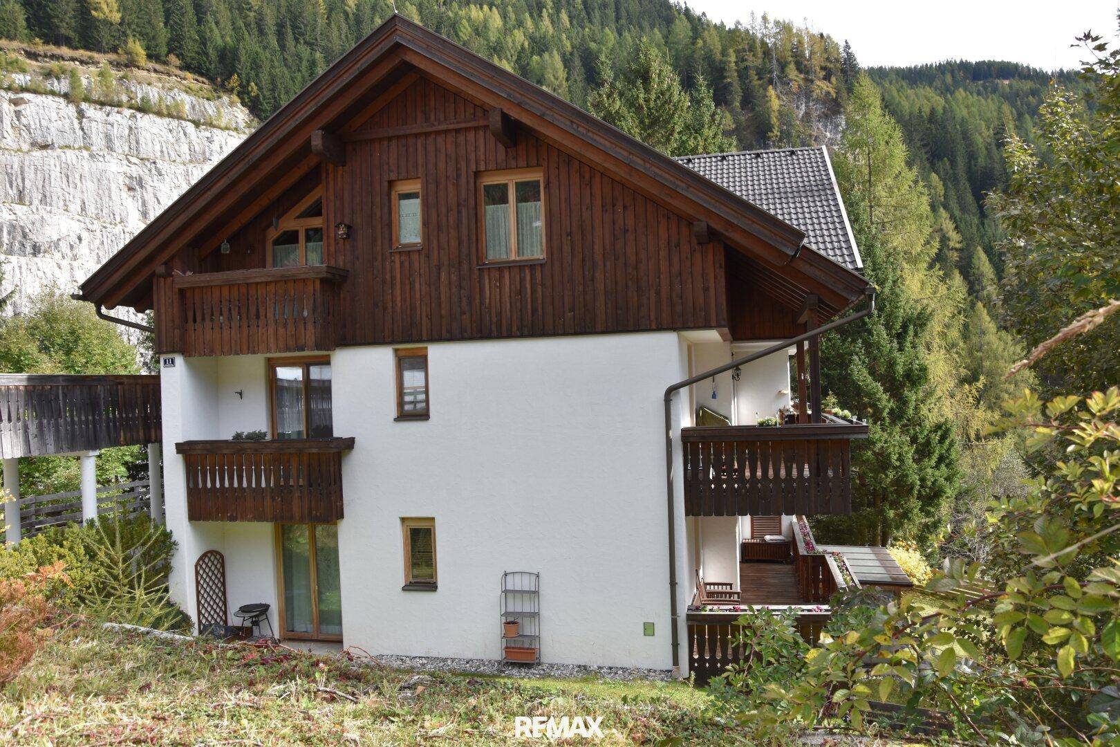 Traditionelles Haus mit Holzfassade und Balkonen, eingebettet in eine grüne Berglandschaft.