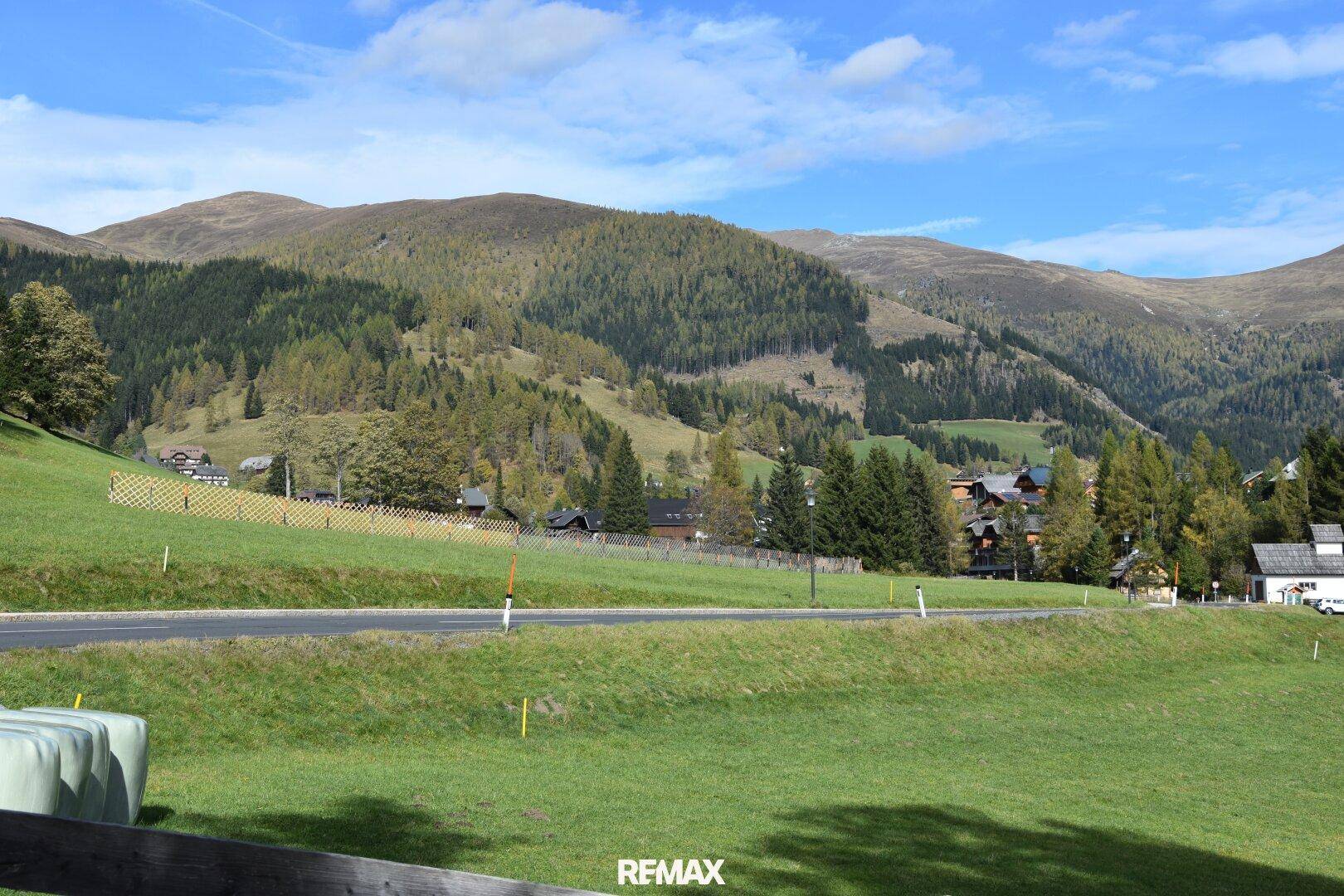Malerische Berglandschaft mit grünen Wiesen und bewaldeten Hängen unter blauem Himmel.