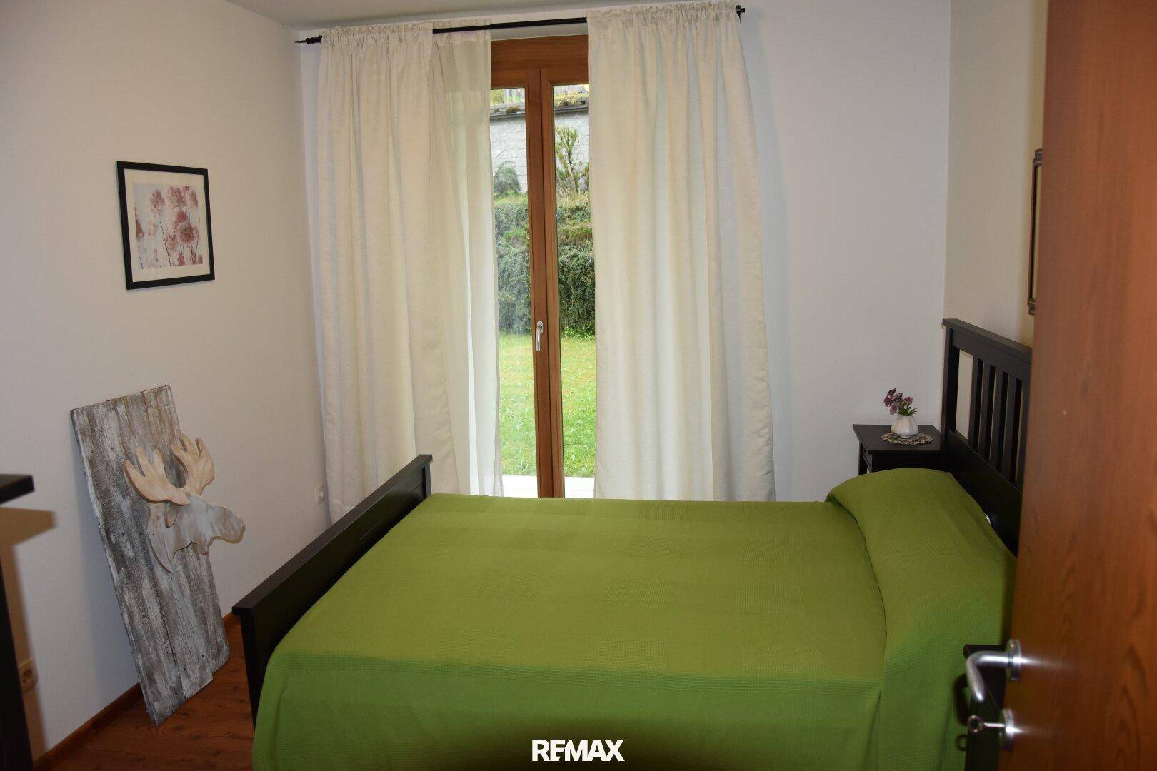 Helles Schlafzimmer mit Zugang zum Garten, ausgestattet mit einem Doppelbett und schlichten Vorhängen.