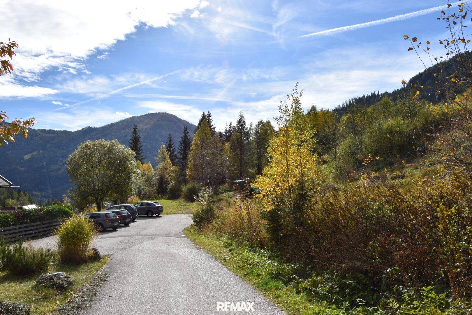 Serpentinenstraße mit Parkplätzen und herbstlicher Vegetation, umgeben von Bergen.