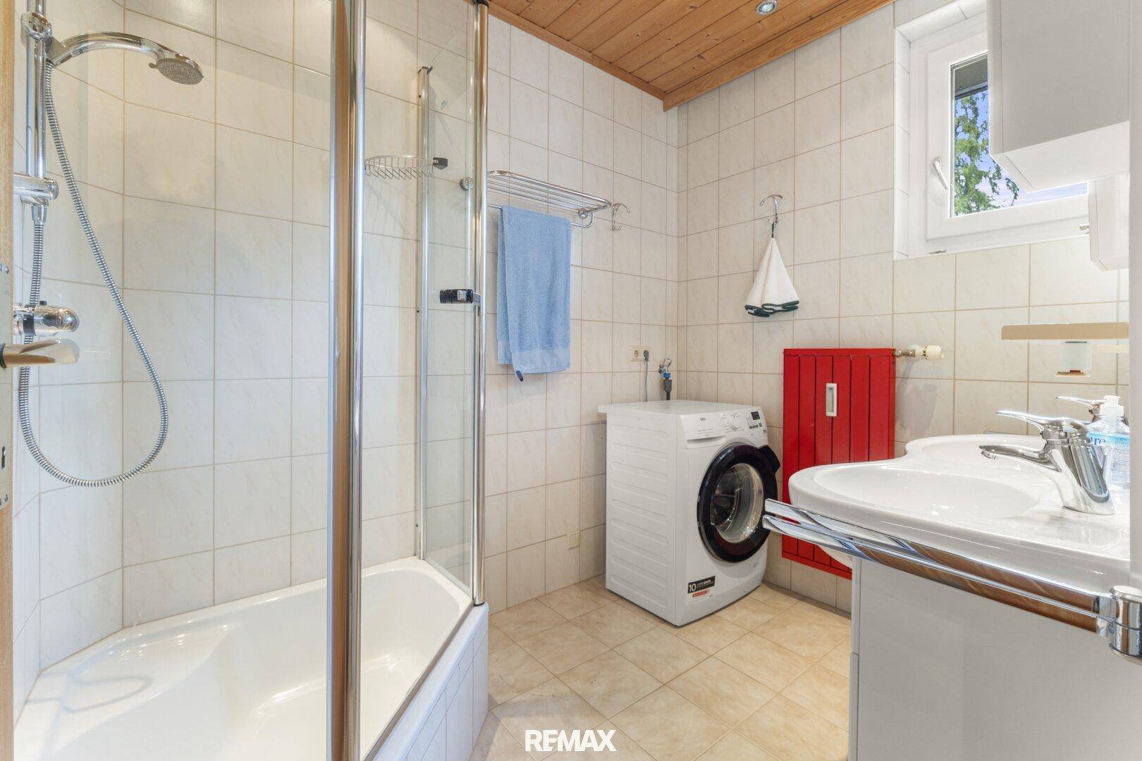 Funktionales Badezimmer mit Duschwanne, Waschbecken, Waschmaschine und Holzdecke.