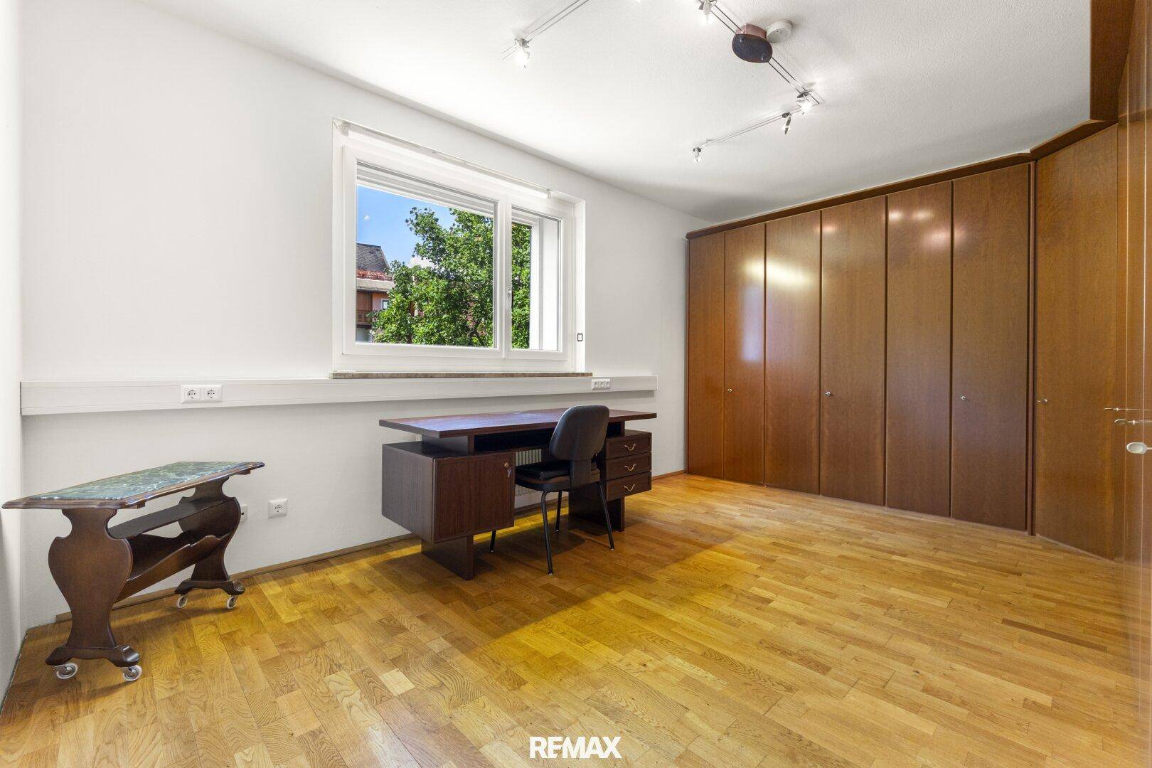 Helles Arbeitszimmer mit Parkettboden, Einbauschränken und Schreibtisch am Fenster.