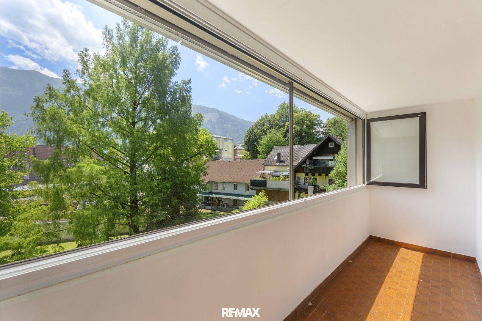 Verglaster Balkon mit Fliesenboden und weitem Blick auf Berge und grüne Umgebung.