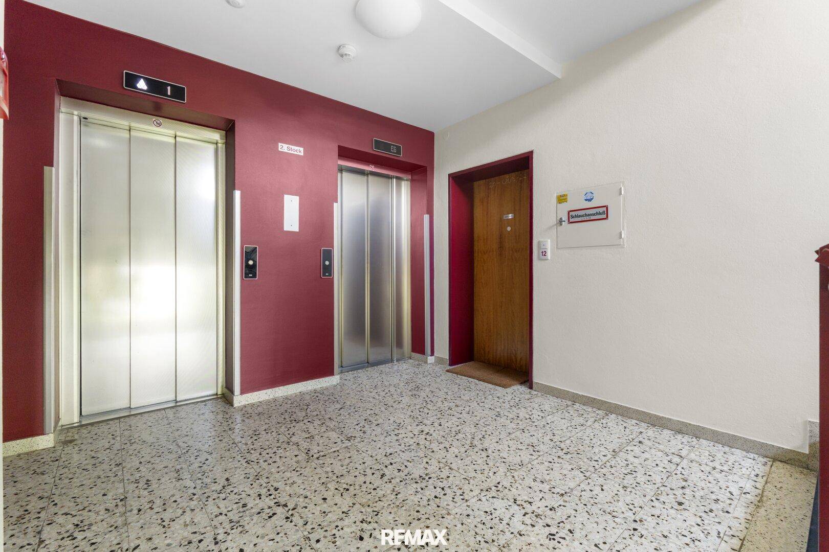 Gemeinschaftlicher Flur mit zwei Aufzügen und einem Terrazzo-ähnlichen Bodenbelag.