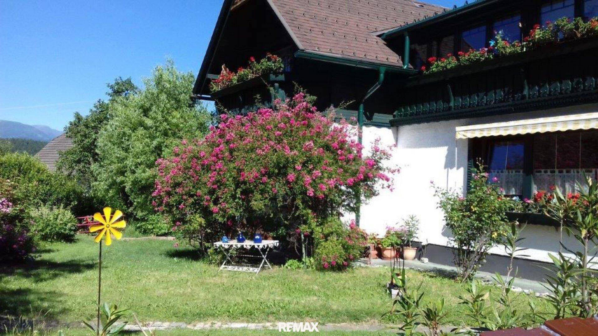 Blühender Gartenbereich mit Sträuchern, Rasenfläche und einem kleinen Tisch.