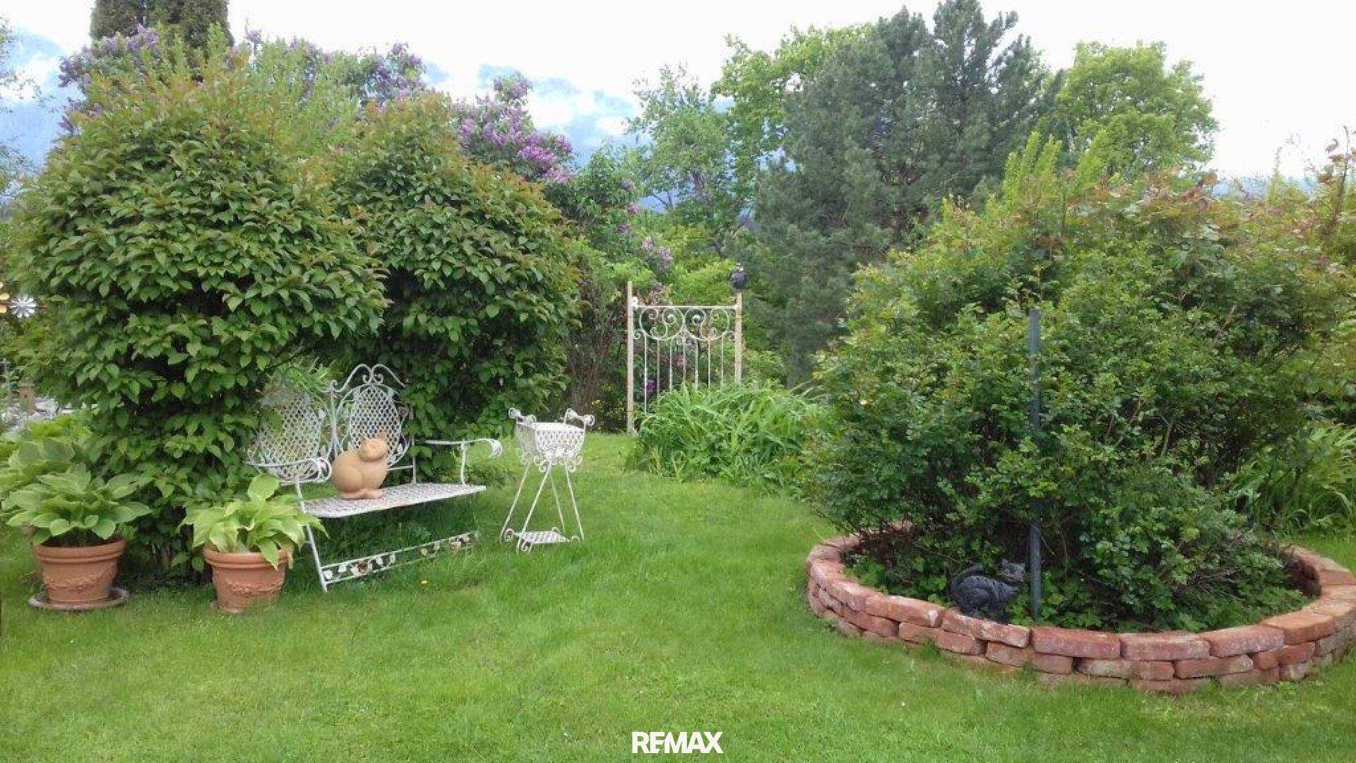 Gepflegter Garten mit Rasenfläche, Ziersträuchern und einer Gartenbank.