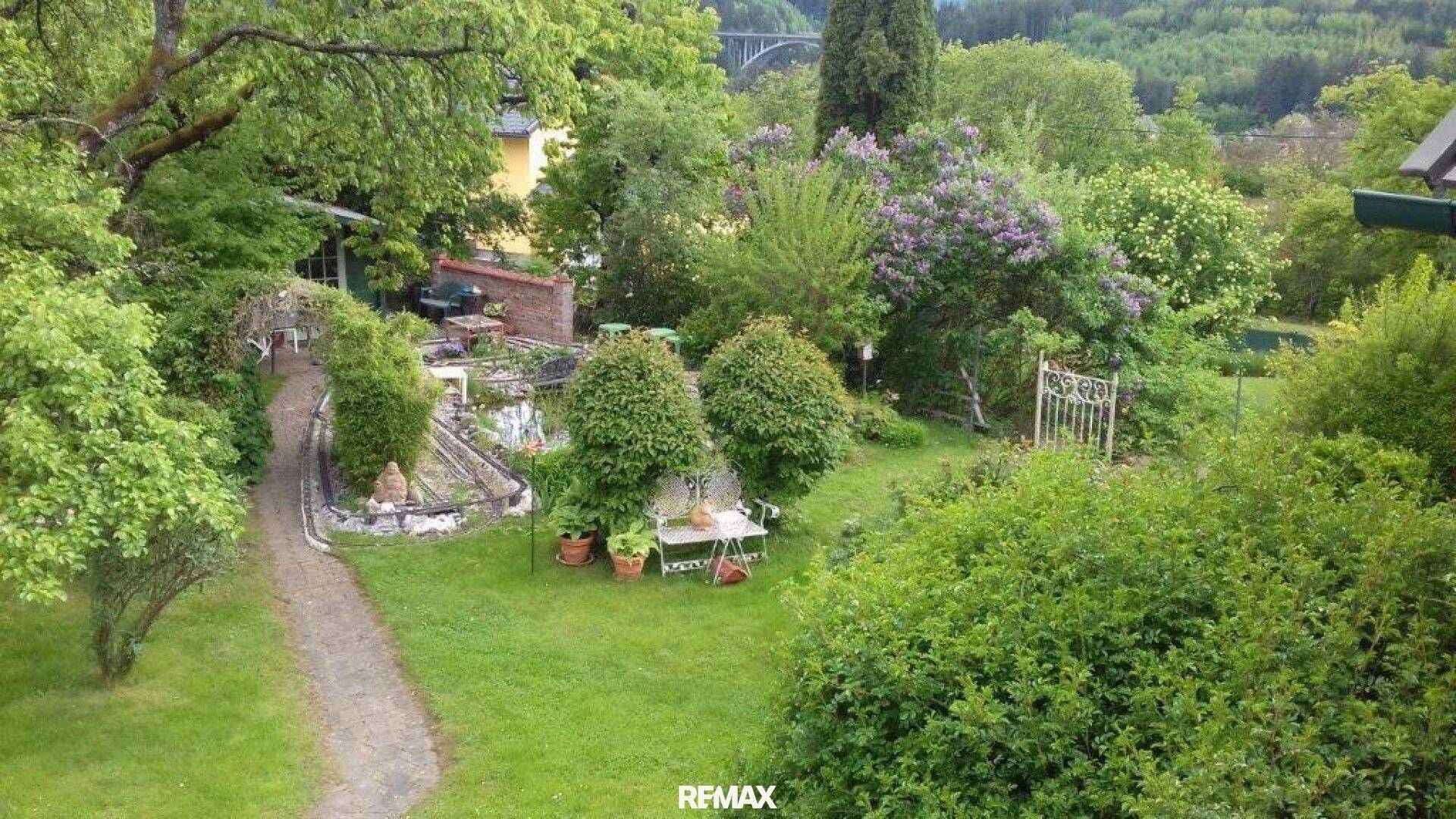 Weitläufiger Garten mit Wegen, Teich und üppiger Vegetation.