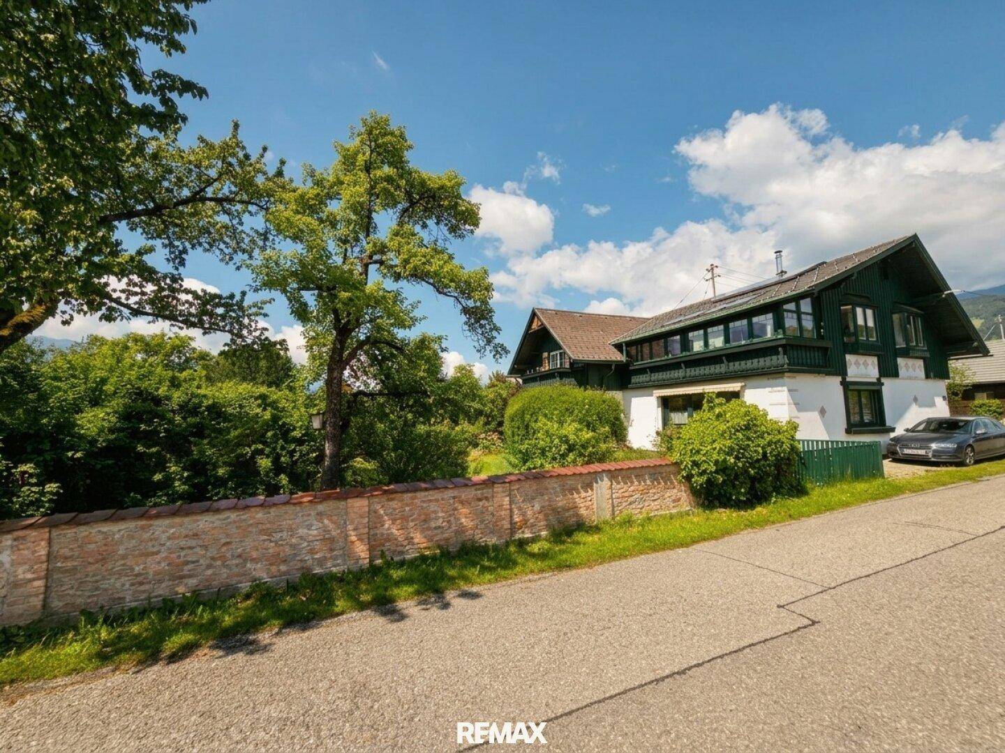 Traditionelles Haus mit grüner Fassade, umgeben von Bäumen und Natur.