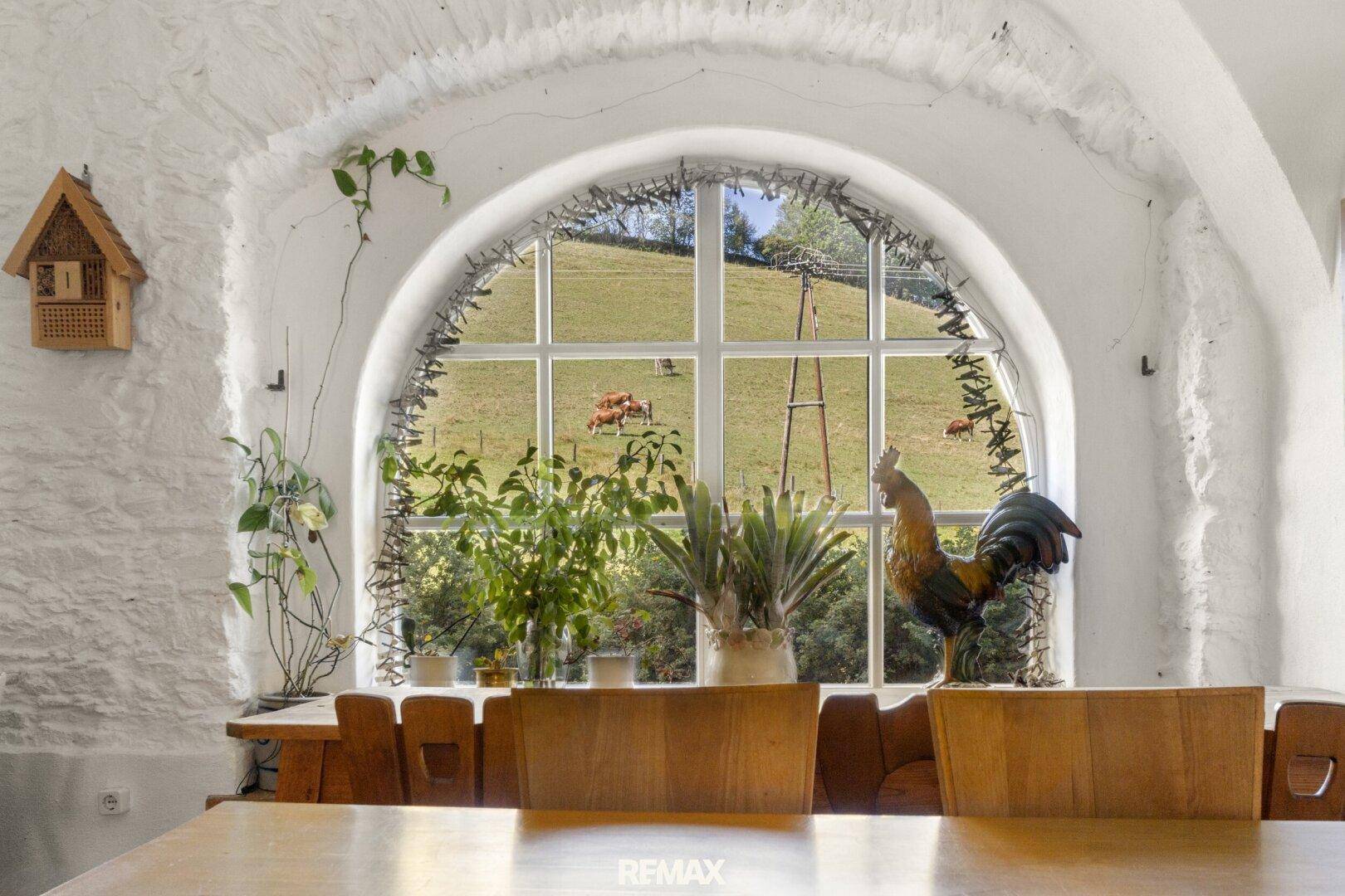 Große Rundbogenfenster bieten einen malerischen Blick auf die grüne Hügellandschaft vom Essbereich.