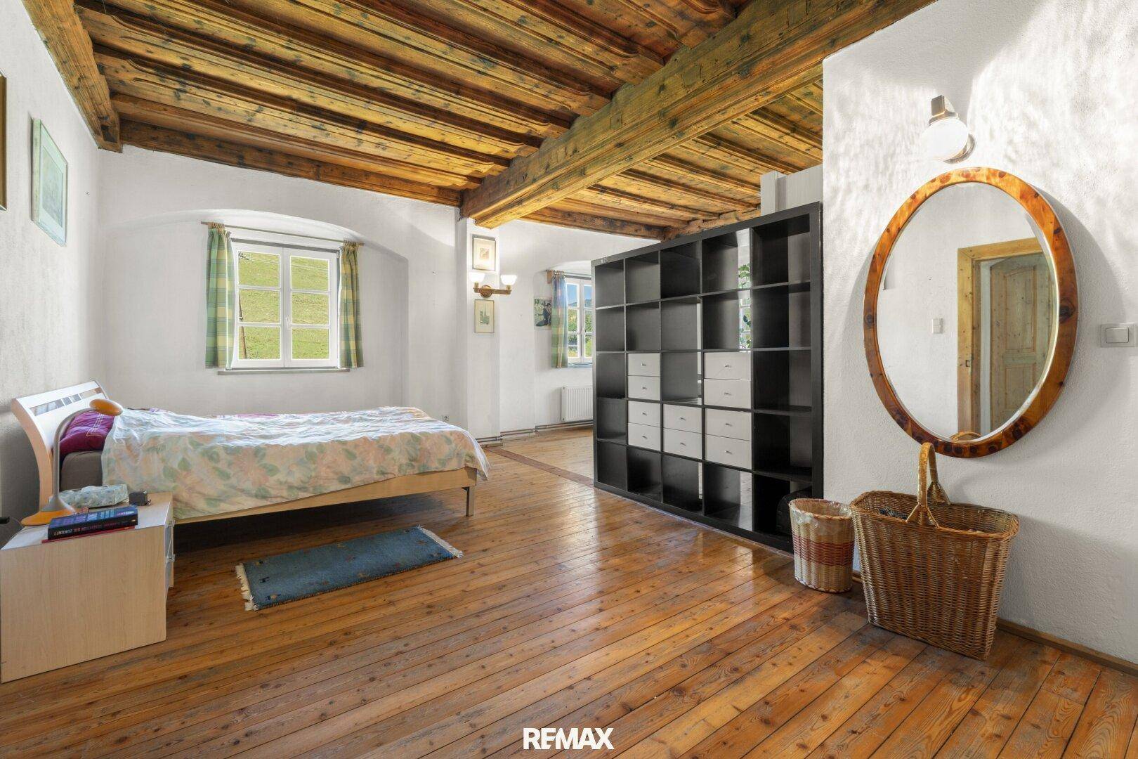 Helles Schlafzimmer mit Holzboden, sichtbaren Deckenbalken und Blick ins Grüne.