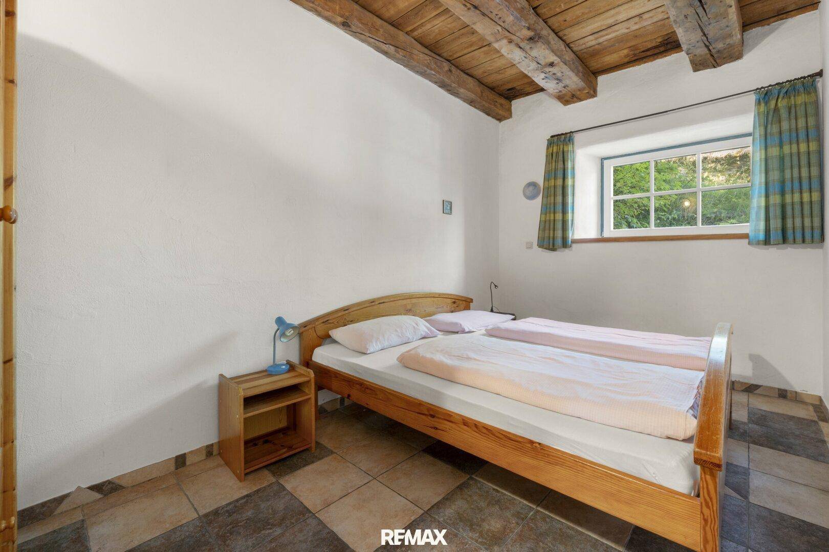 Einfaches Schlafzimmer mit Holzbett und karierten Fliesen, bietet einen ruhigen Rückzugsort.