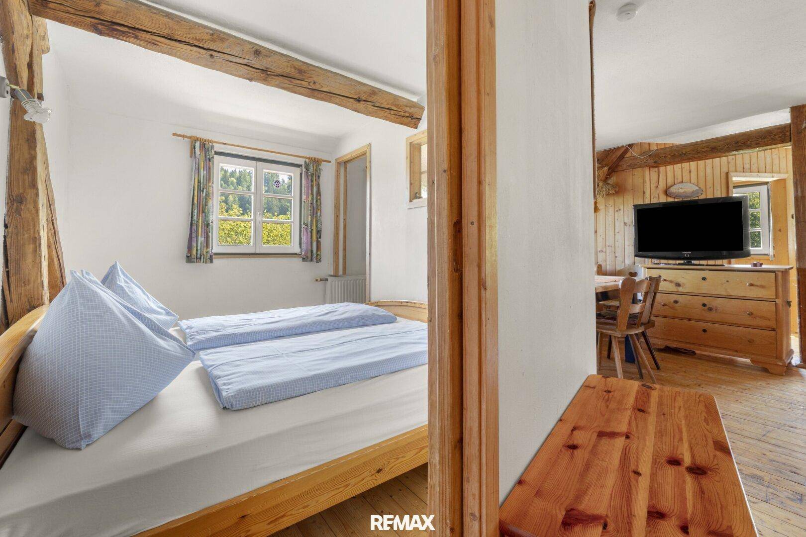 Schlafzimmer mit Holzbett und Blick auf den angrenzenden Wohnbereich mit Holzbalken.