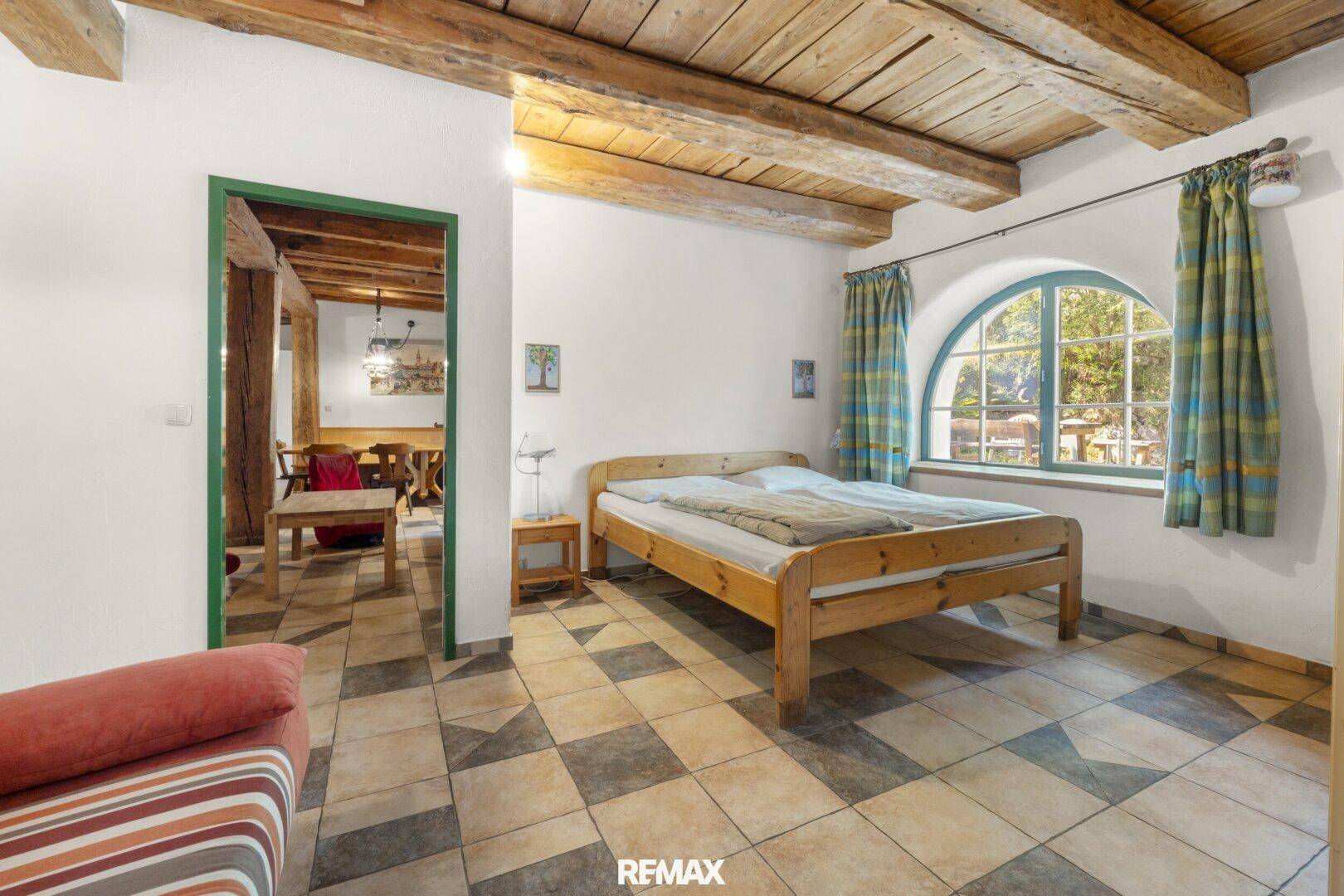 Schlafzimmer mit Holzbett und karierten Fliesen, angrenzend an einen weiteren Wohnbereich.