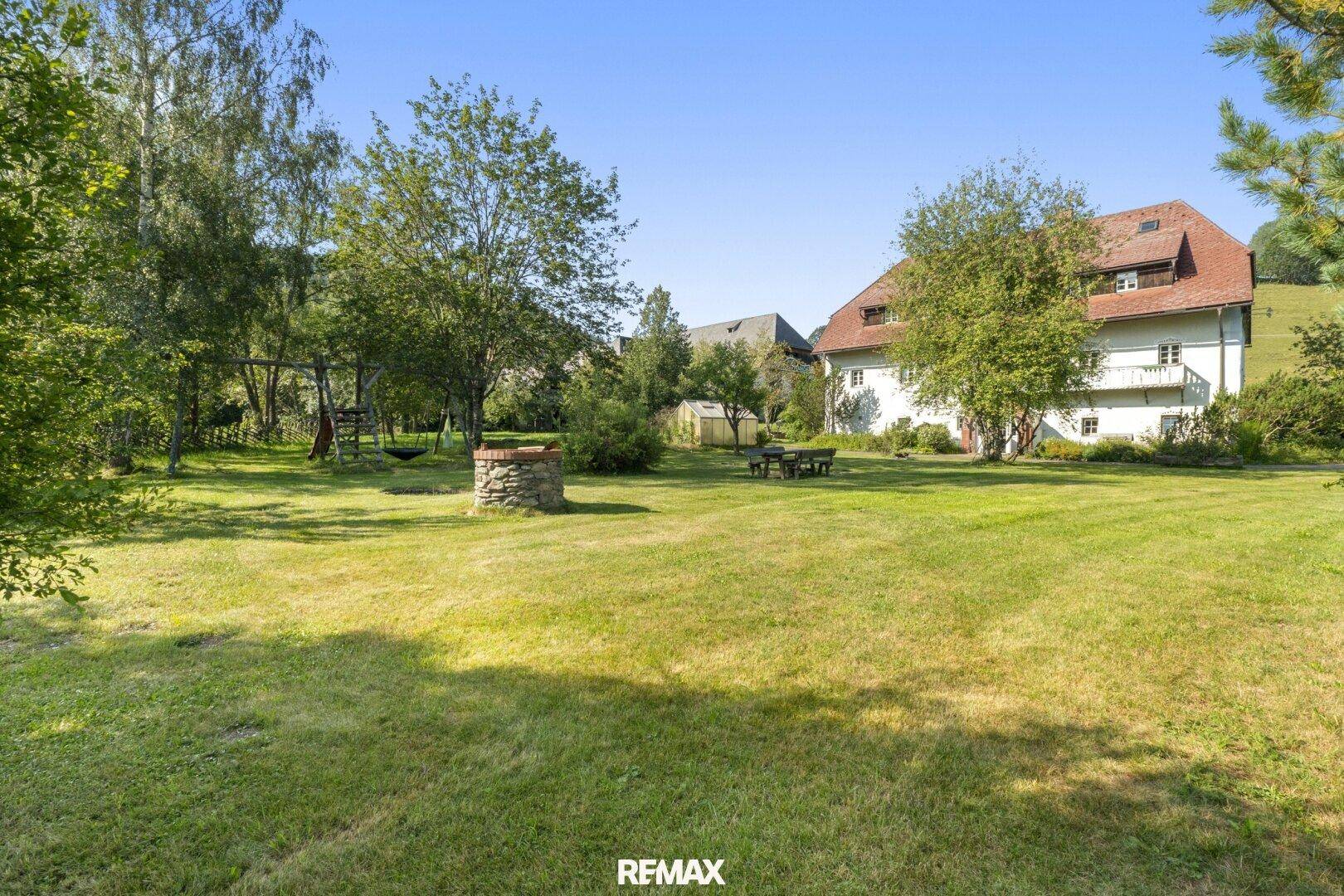 Großer, gepflegter Garten mit Rasenfläche, Bäumen und einem Brunnen, ideal zum Entspannen.