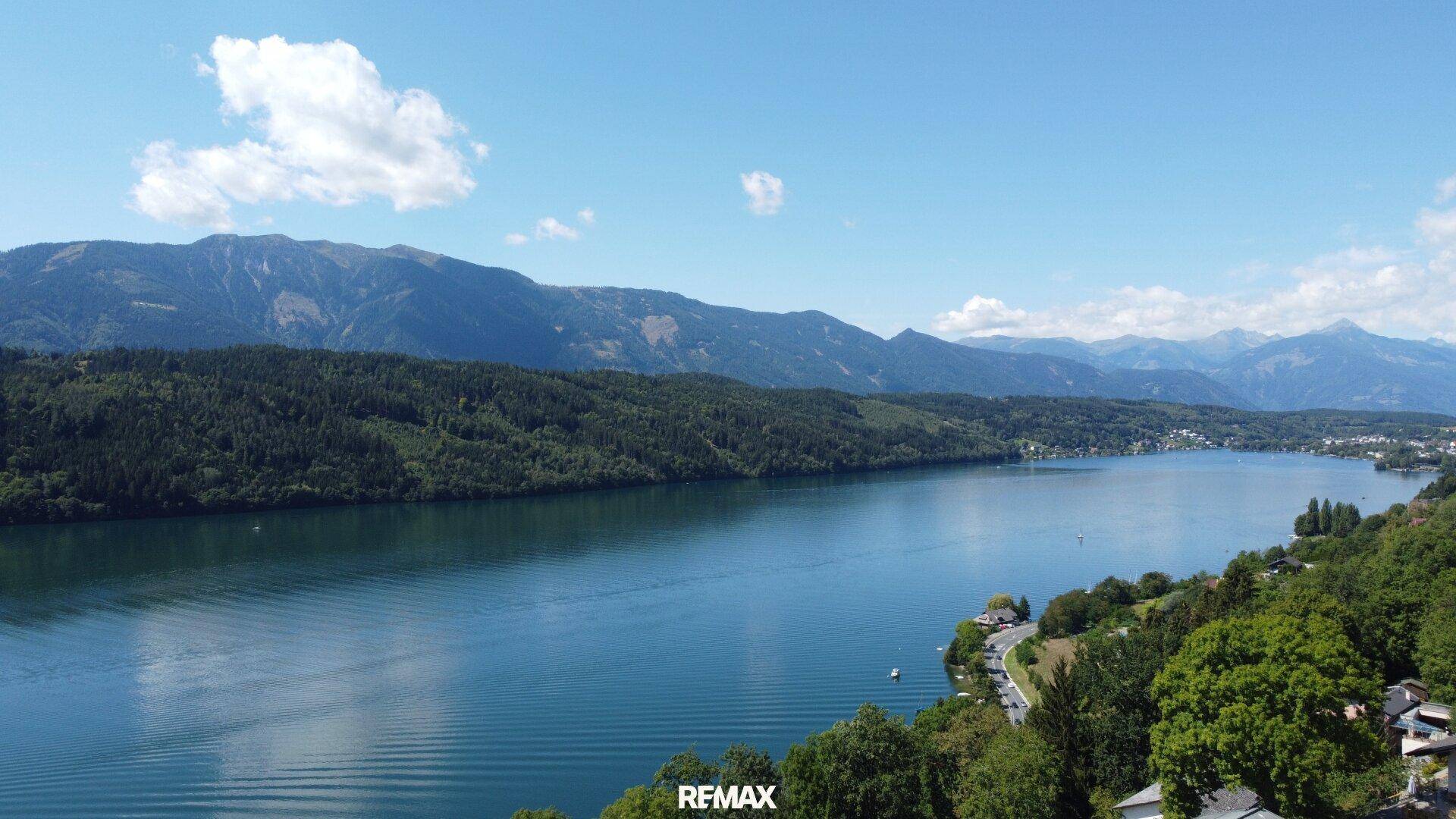 Malerischer Panoramablick über den See und die umliegende Berglandschaft an einem sonnigen Tag.