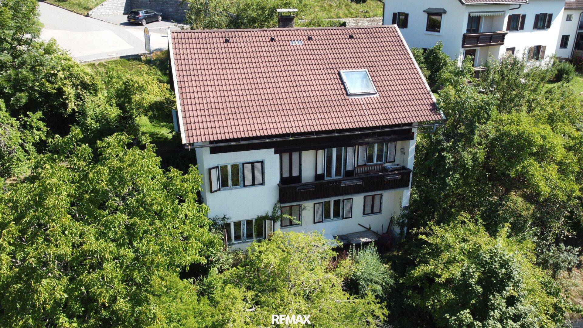 Ansicht des Hauses von oben mit weißer Fassade, rotem Ziegeldach und umgebender grüner Vegetation.