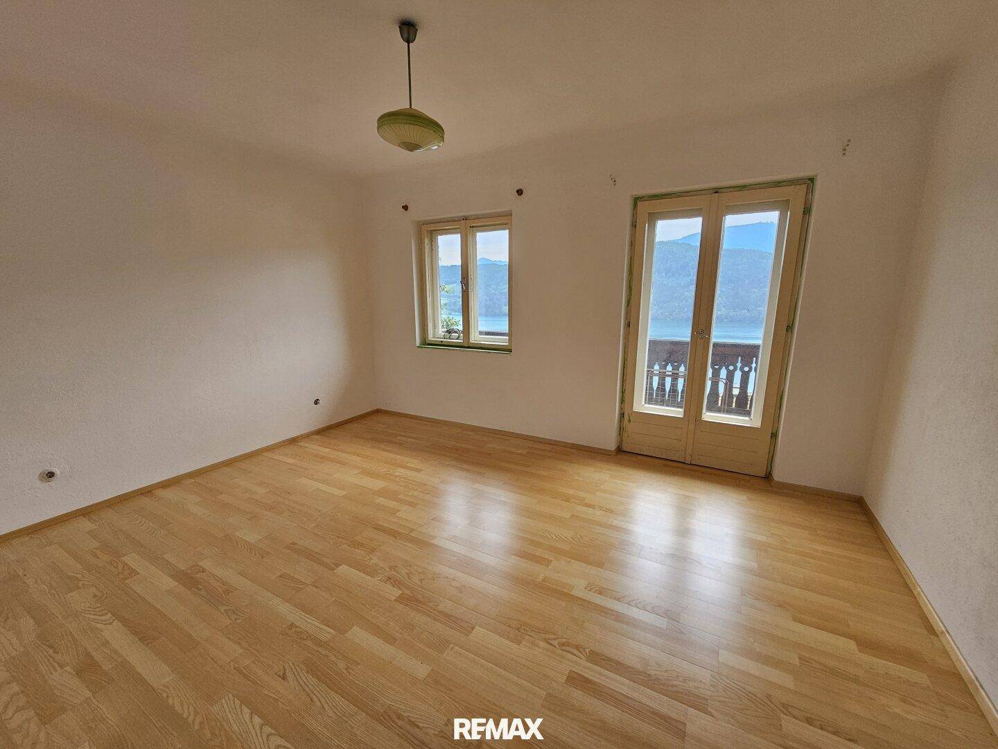 Helles Zimmer mit Holzboden, Balkonzugang und weitem Blick auf den See und die Berge.