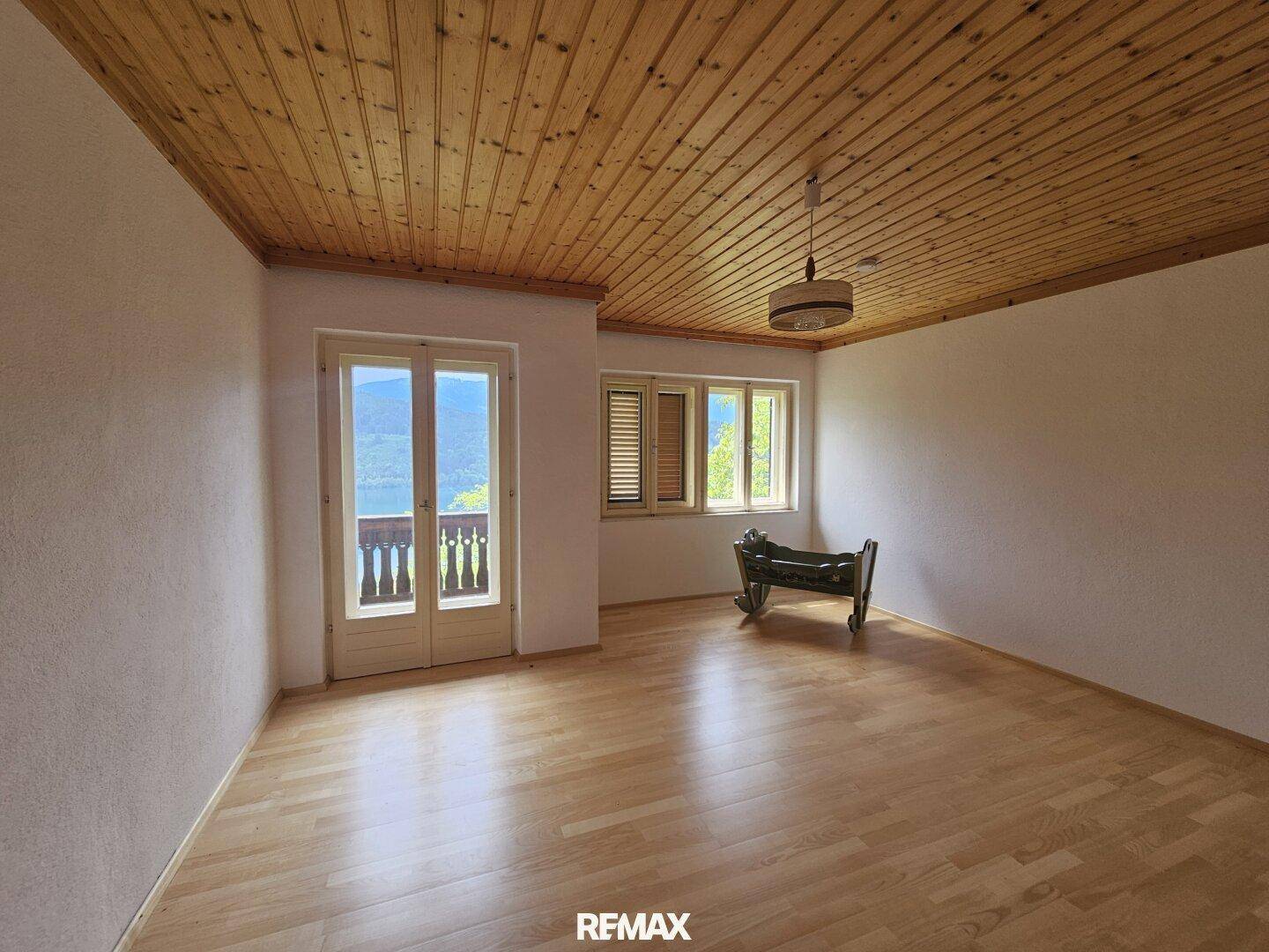 Geräumiges Zimmer mit Holzboden, Holzdecke und Balkonzugang mit Blick auf die Umgebung.