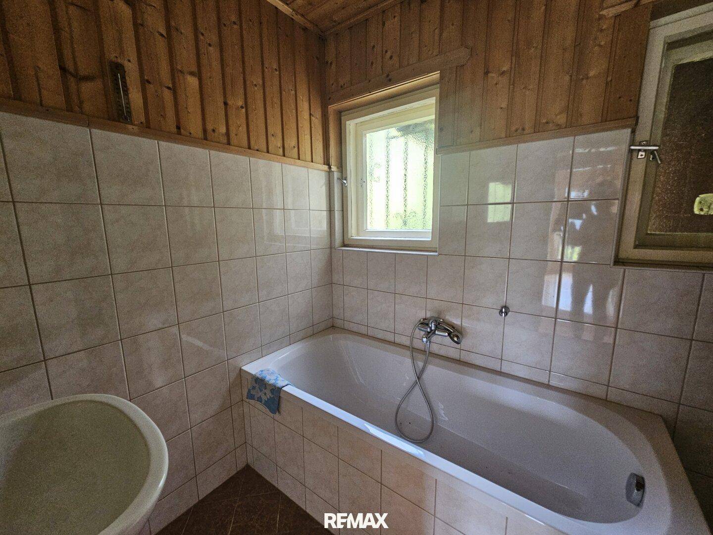 Badezimmer mit Badewanne, hellen Fliesen an den Wänden und einer rustikalen Holzdecke.