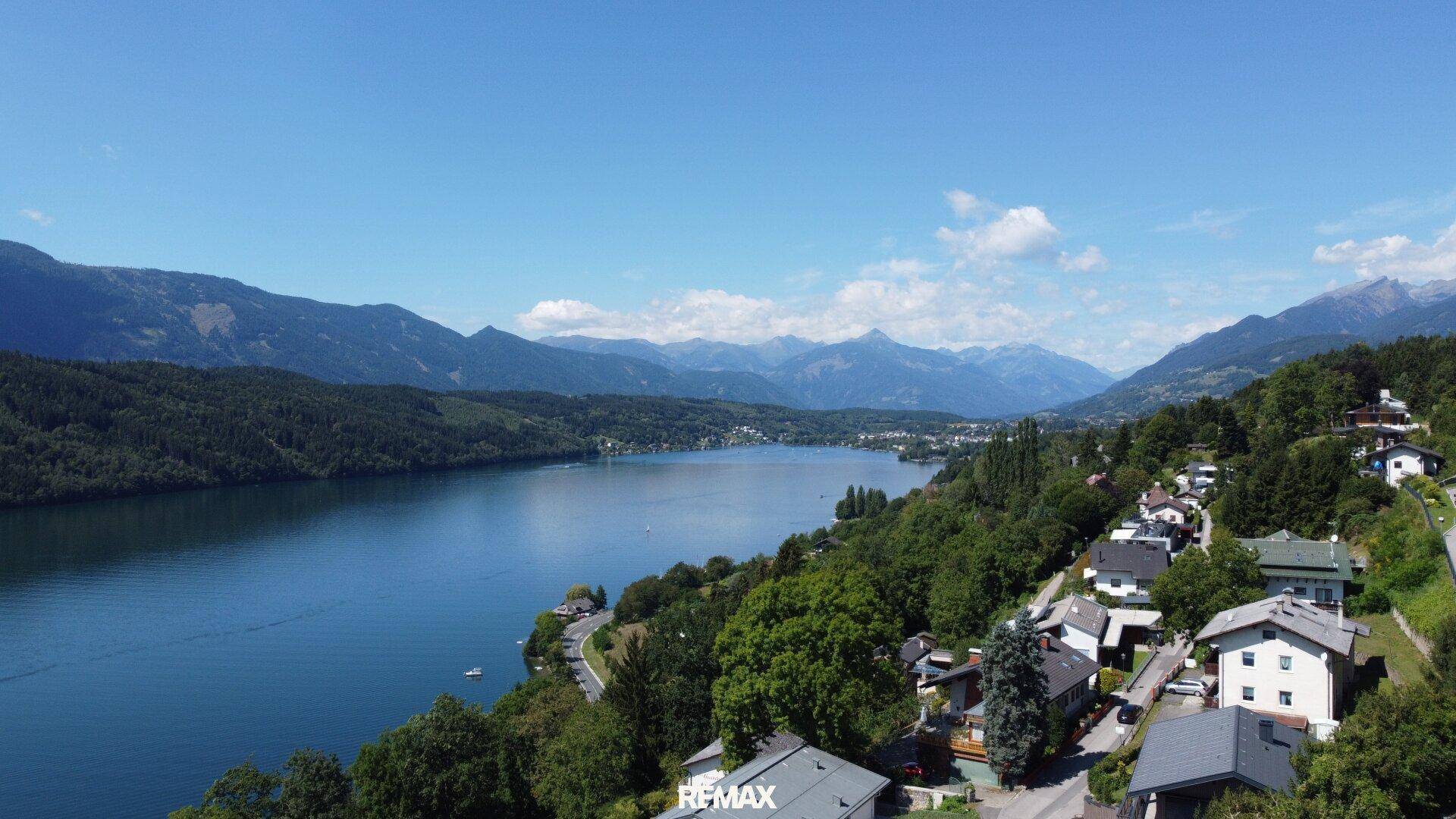 Panoramablick auf die malerische Seenlandschaft mit umliegenden Bergen und Uferbebauung.