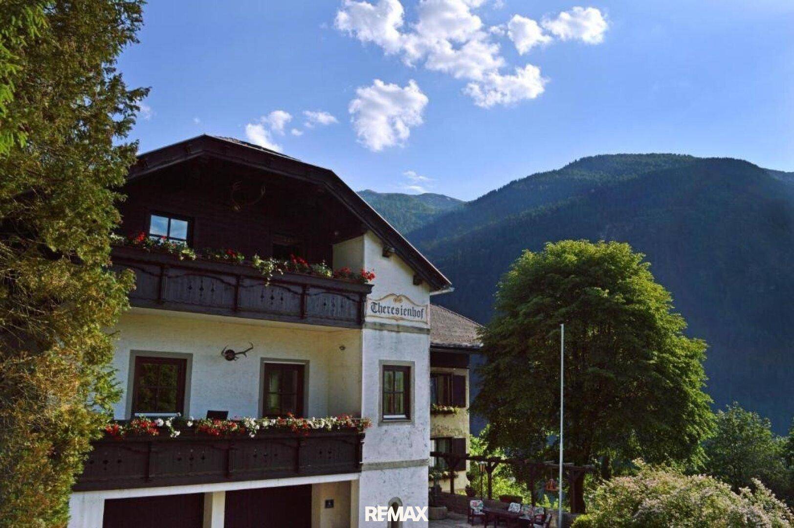 Charmantes Alpenhaus mit traditionellen Holzbalkonen und Blumenkästen vor einer bergigen Kulisse.
