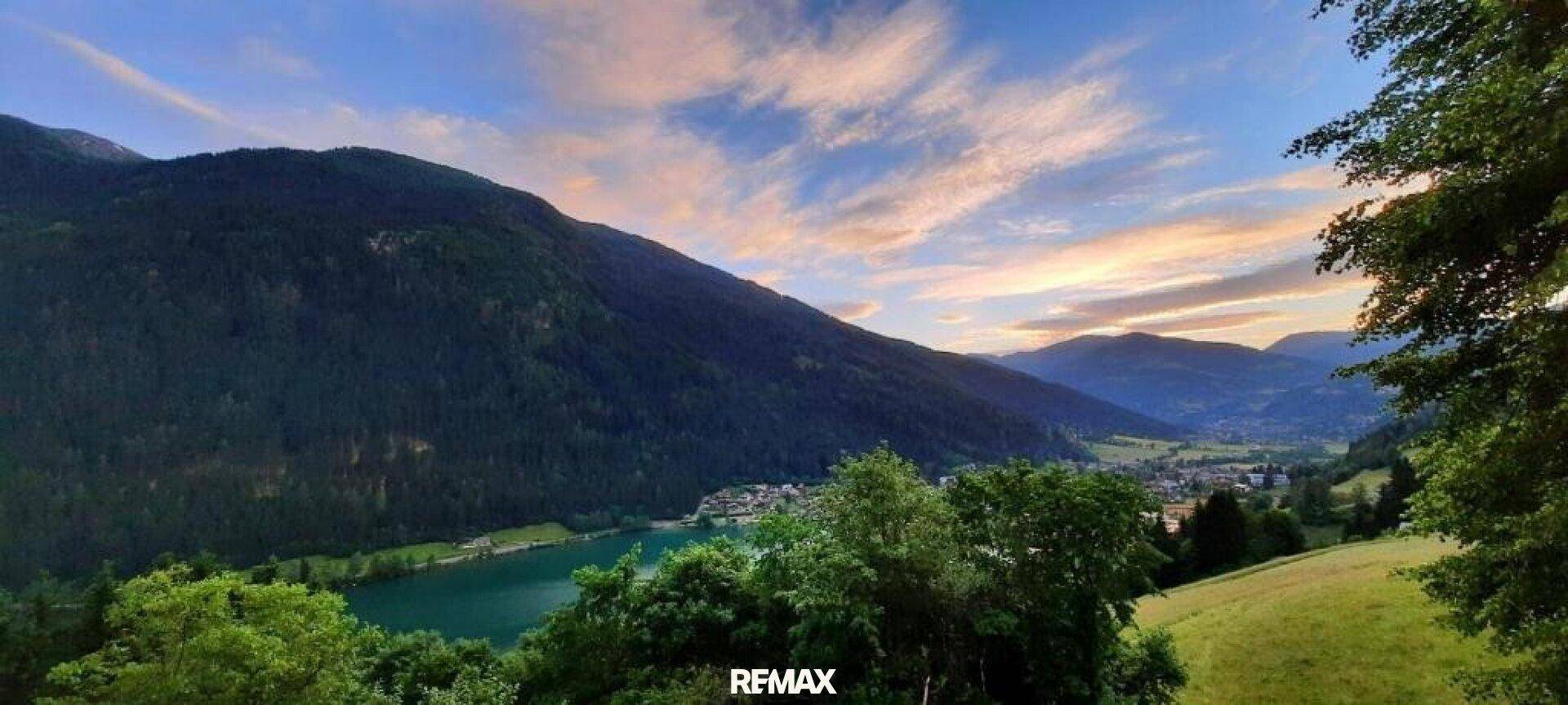 Atemberaubender Sonnenuntergang über einem ruhigen See, eingebettet in eine Berglandschaft mit sanften Wolken.