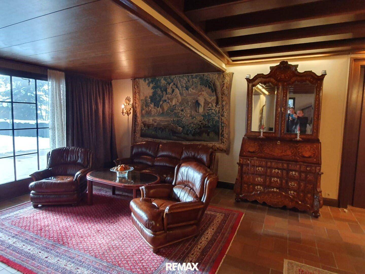 Gemütliches Wohnzimmer mit Ledersofas, einem Wandteppich und dunklen Holzbalken an der Decke.