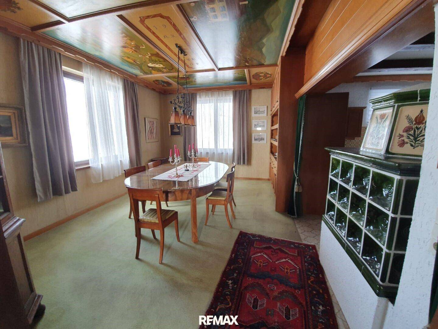 Traditionelles Esszimmer mit bemalter Holzdecke, Kachelofen und einem großen Esstisch.