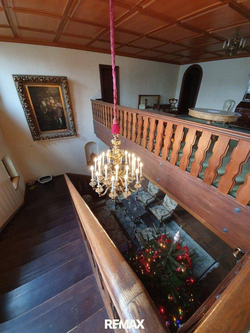 Prunkvolles Treppenhaus mit Holzgeländer und einem großen Kronleuchter, der den Raum erhellt.
