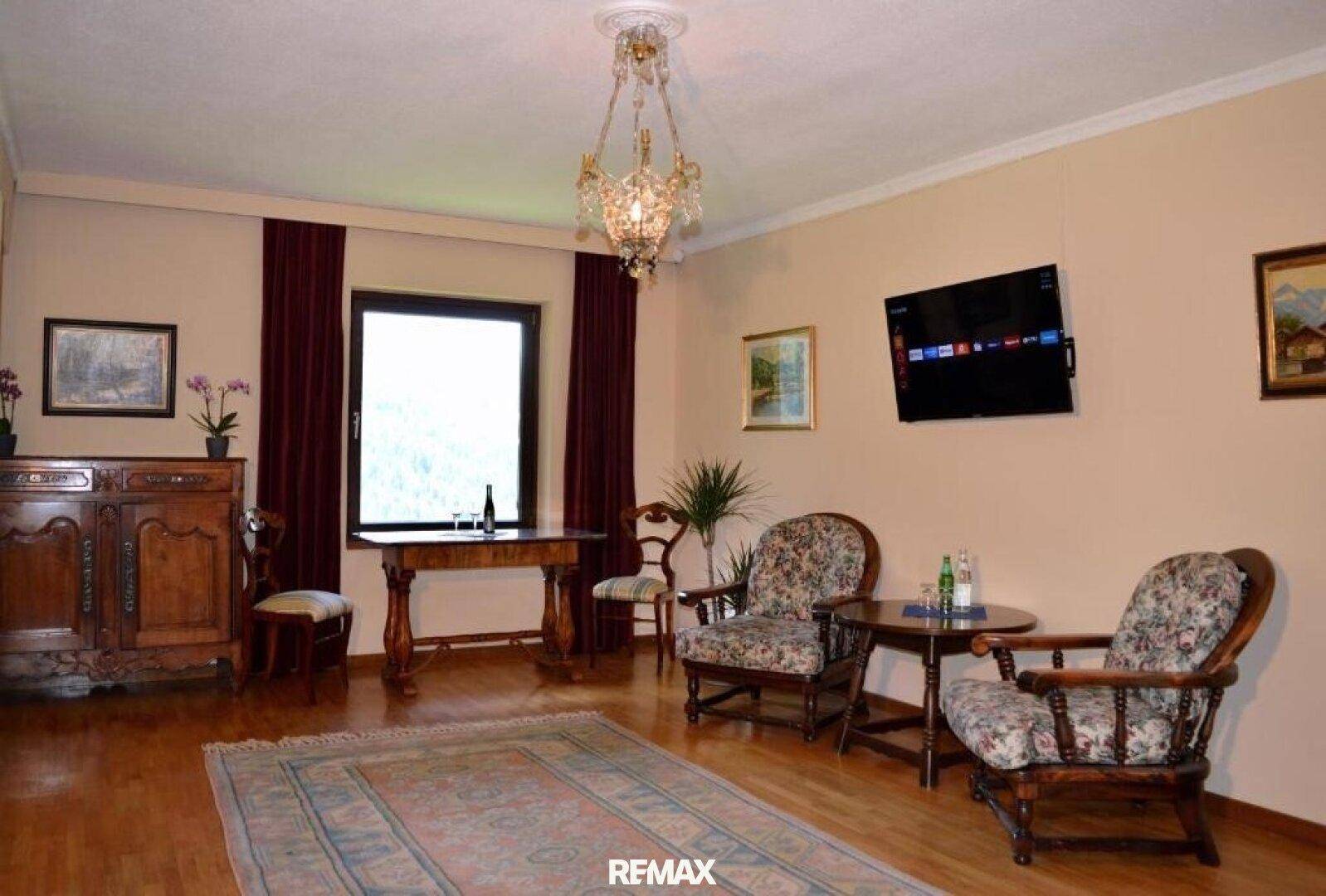 Gemütlicher Wohnbereich mit floral gemusterten Sesseln, Holztisch und einem Fernseher an der Wand.