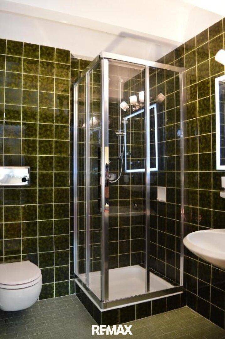 Badezimmer mit grünen Fliesen, Duschkabine, WC und Waschbecken, in einem traditionellen Stil.