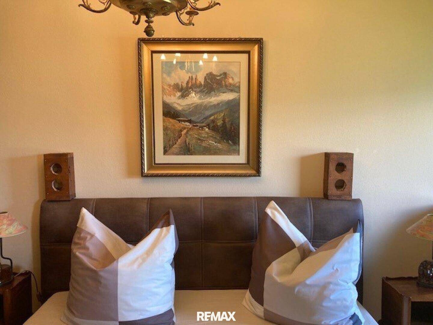 Detailansicht eines Bettes mit Kissen und einem gerahmten Bergbild über dem Kopfteil.