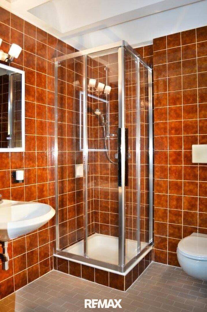 Badezimmer mit braunen Fliesen, Duschkabine, WC und Waschbecken, in einem warmen Farbton.