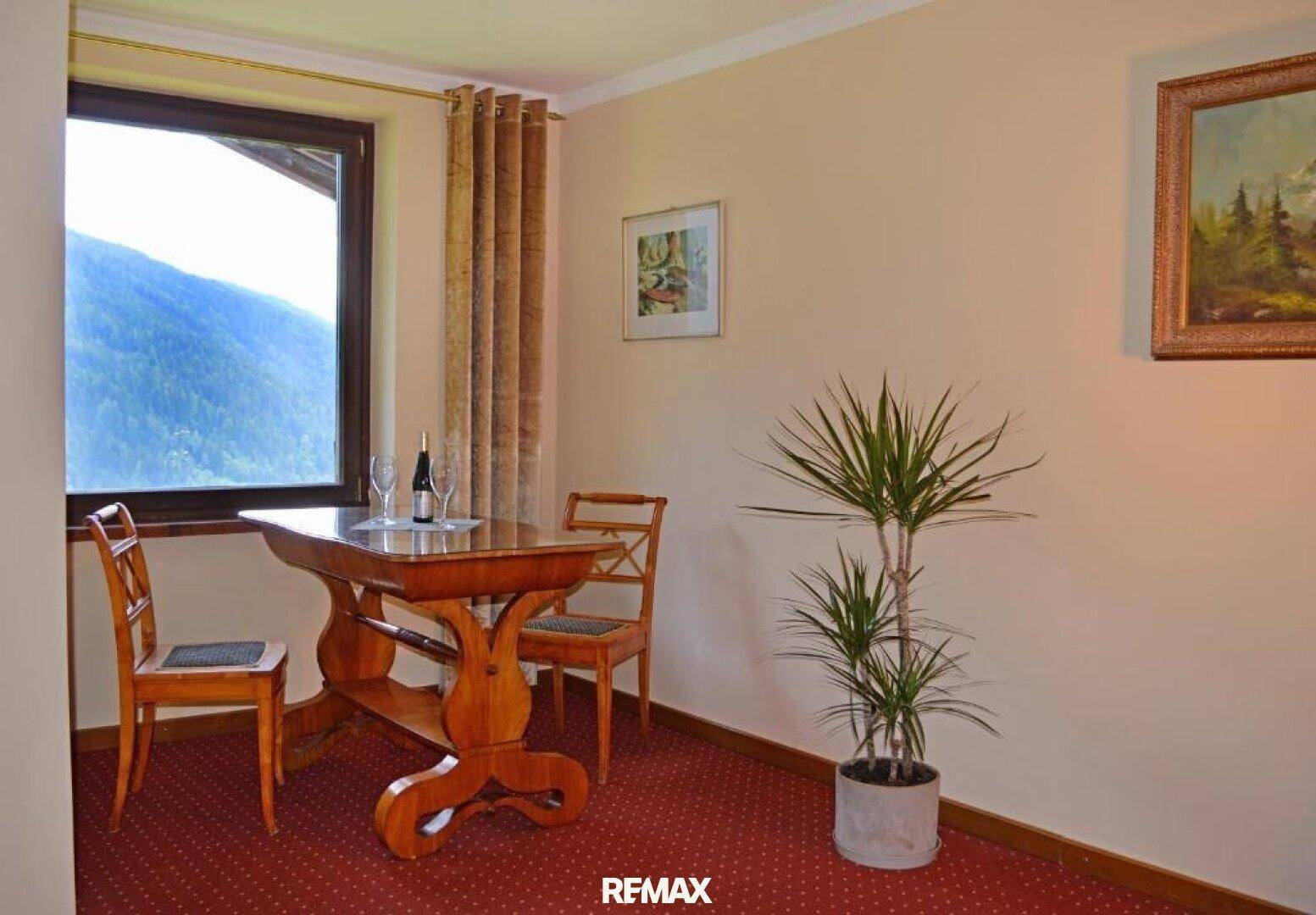 Kleiner Essbereich mit Holztisch und Stühlen, umgeben von hellen Wänden und einem Fenster mit Bergblick.