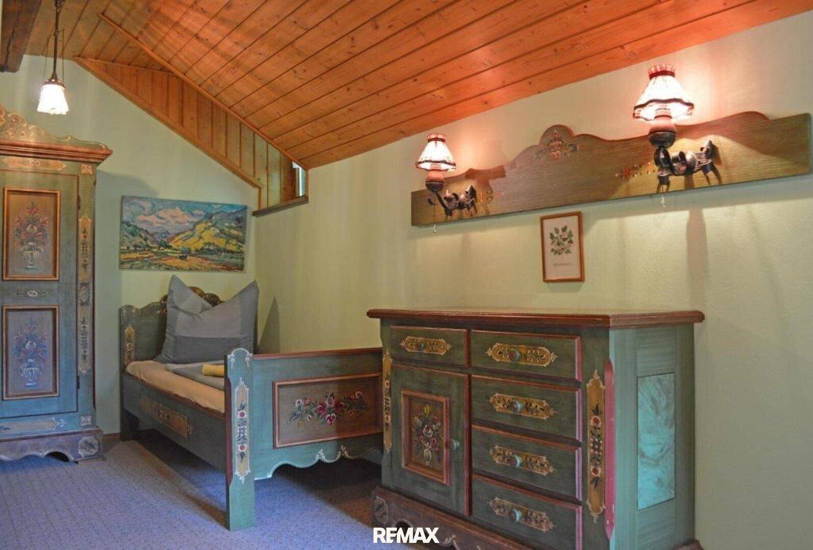 Rustikales Schlafzimmer mit handbemalten Holzmöbeln, Einzelbett und schräger Holzdecke.