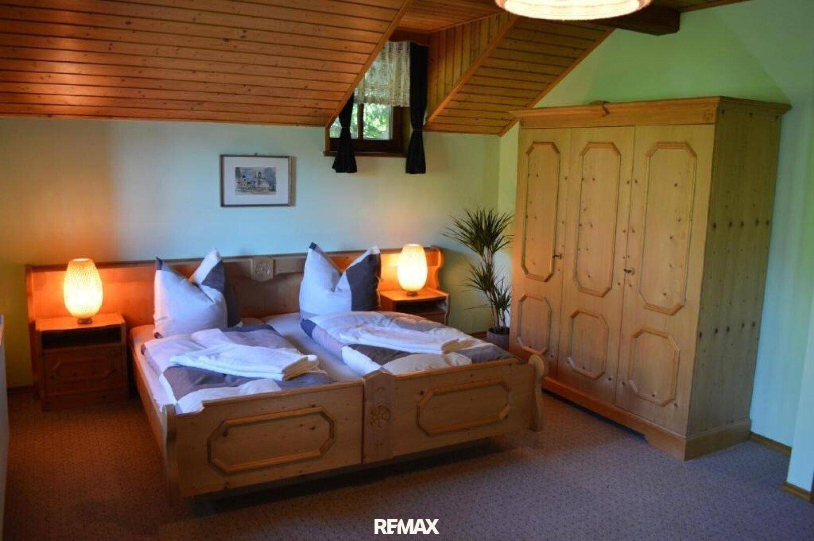 Helles Schlafzimmer mit zwei Einzelbetten, Kiefernholzmöbeln und schräger Holzdecke.