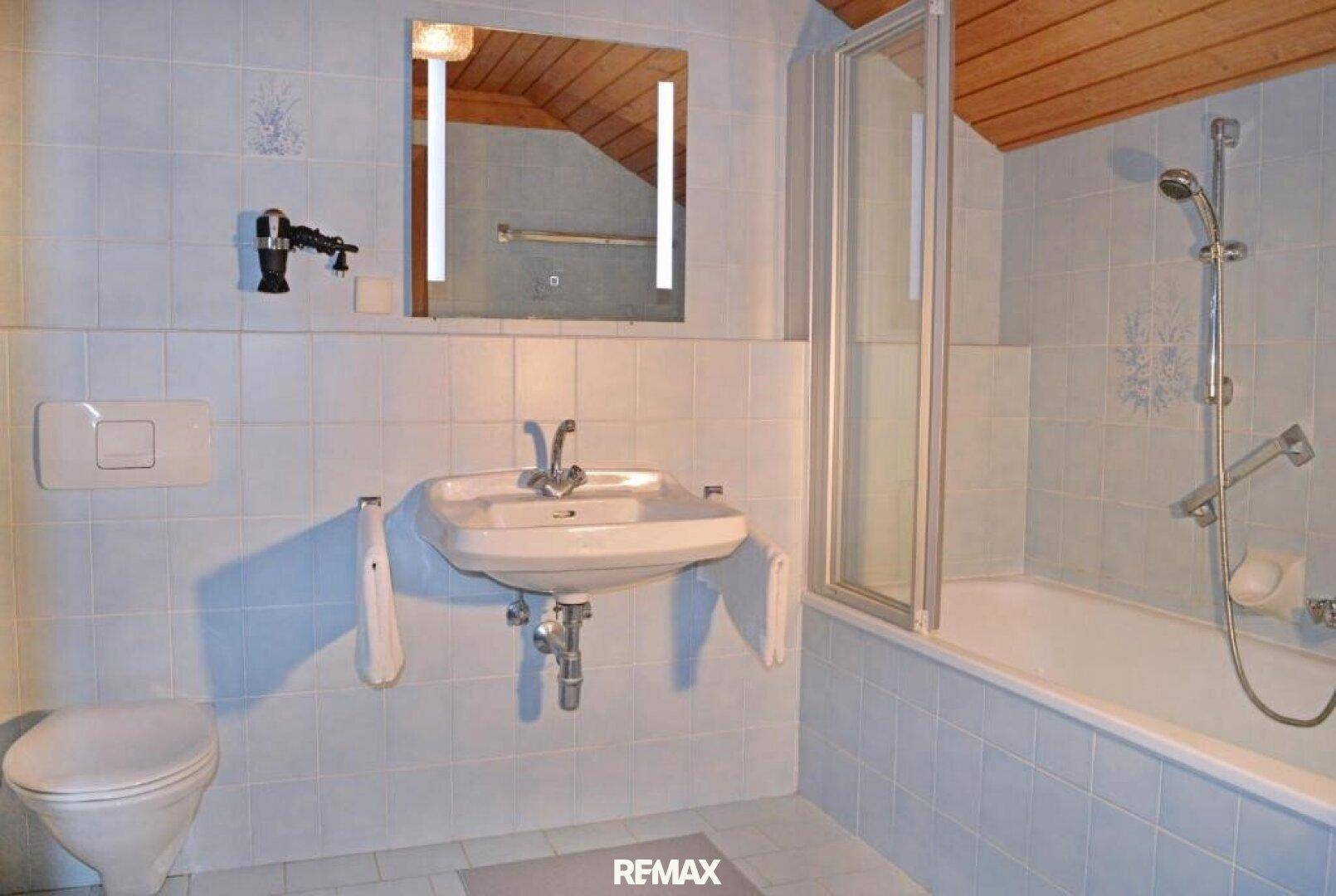 Badezimmer mit hellblauen Fliesen, Badewanne mit Duschfunktion und Holzdecke.