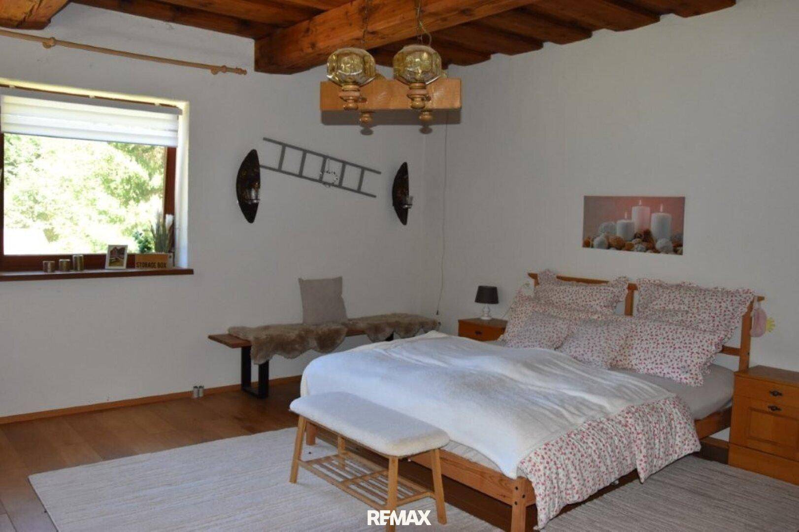 Schlafzimmer mit Holzbalkendecke, Doppelbett und Fenster mit Blick auf die Natur.