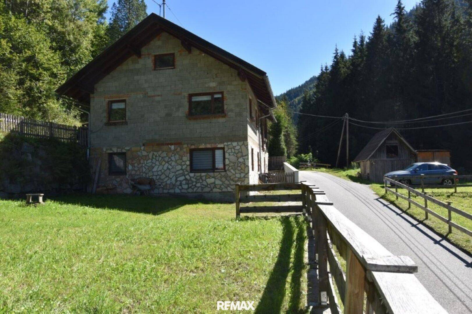 Ländliches Haus mit Steinfassade und Holzelementen an einer kleinen Straße in den Bergen.