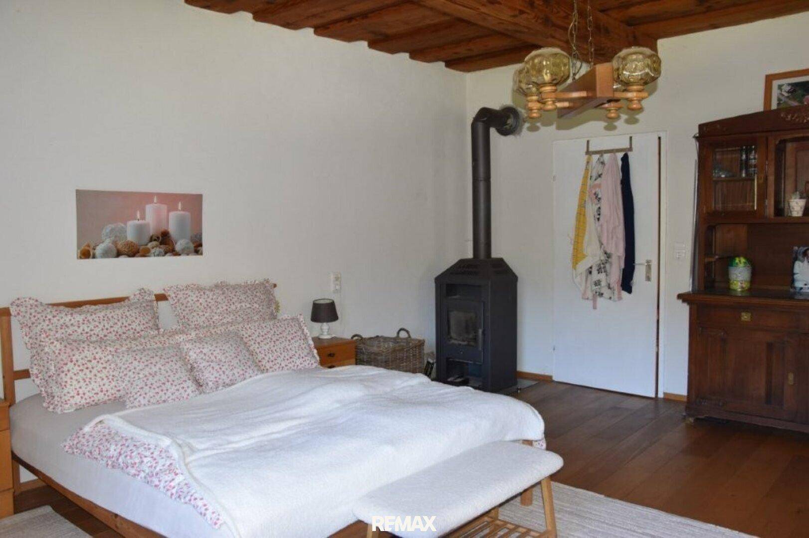 Schlafzimmer mit Holzbalkendecke, Kaminofen und traditionellem Holzschrank.