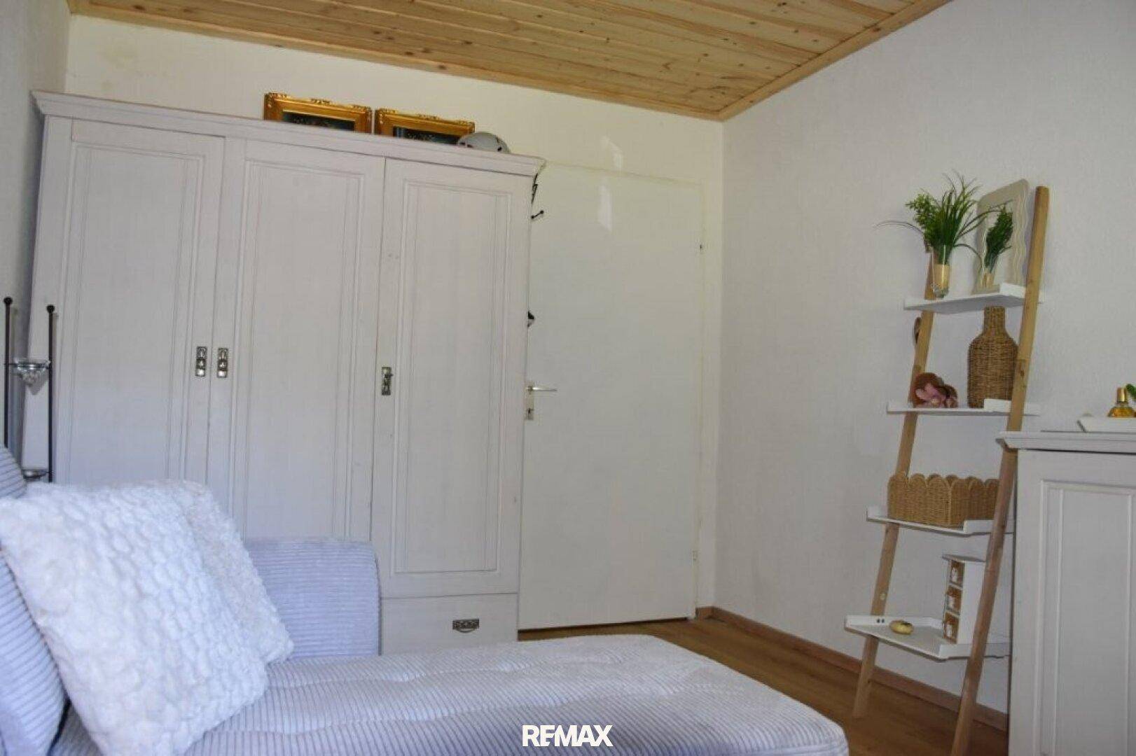 Schlafzimmer mit Holzdecke, weißem Kleiderschrank und Chaiselongue.