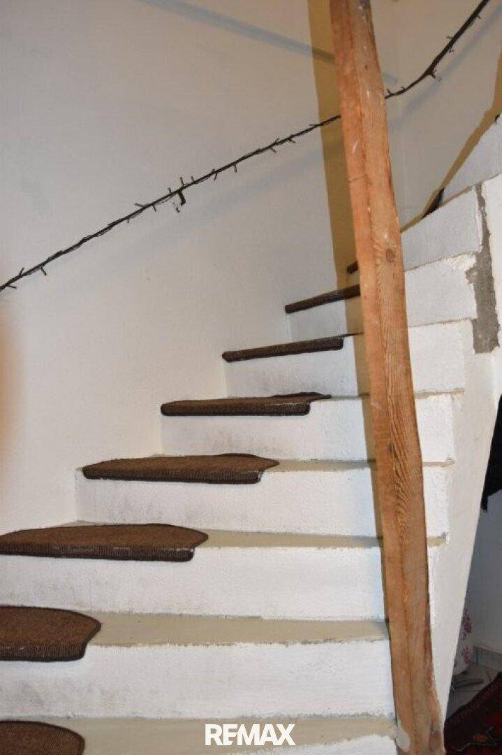 Einfache Treppe mit weißen Stufen und braunen Teppichauflagen, rustikales Geländer.