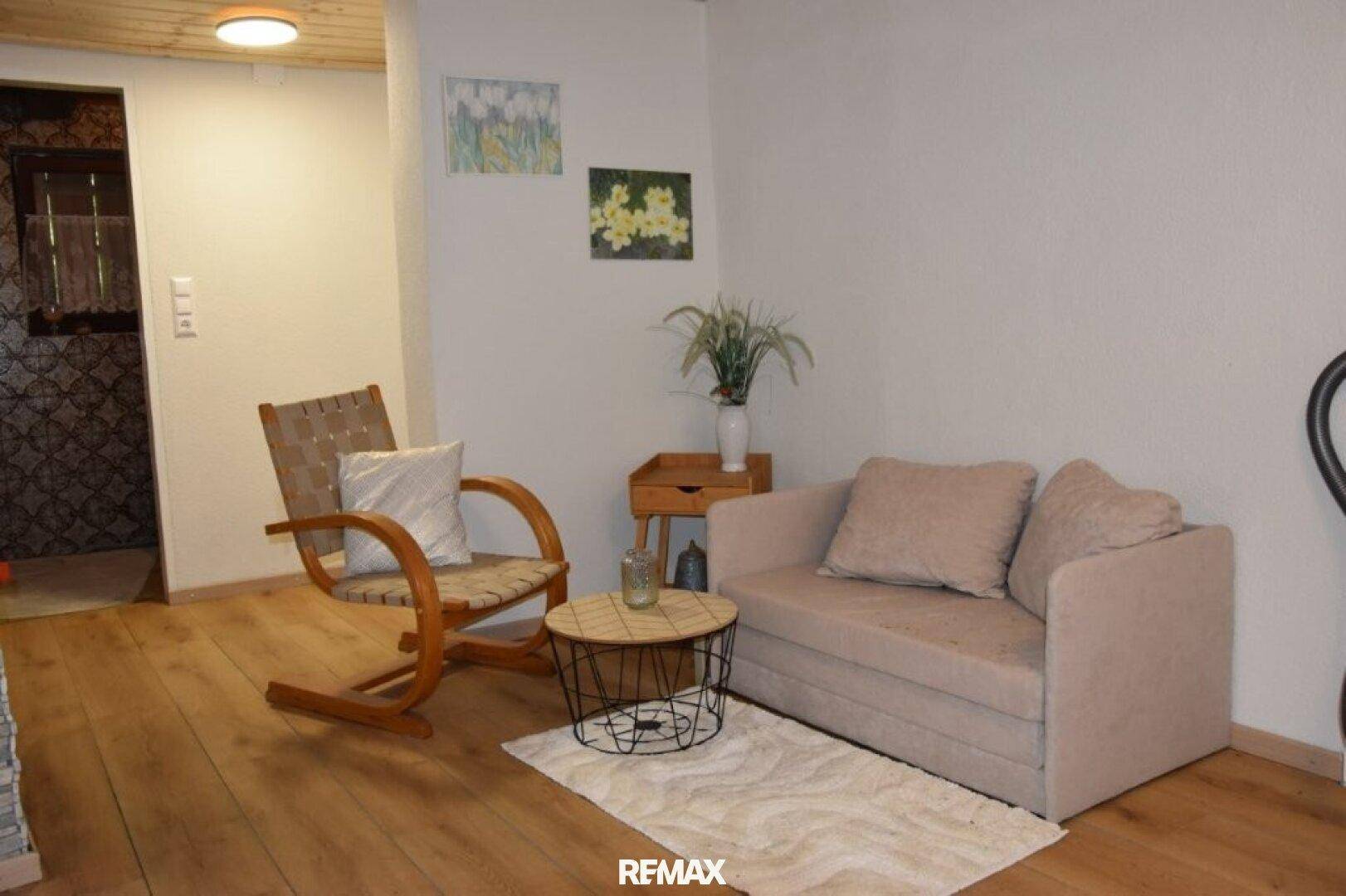 Gemütliches Wohnzimmer mit Holzboden, beigem Sofa und Sessel, dekoriert mit Pflanzen.
