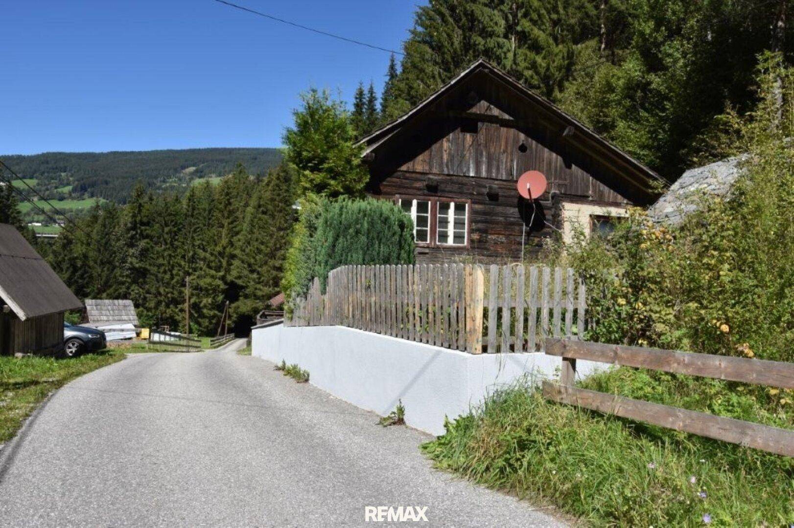 Rustikales Holzhaus mit Satteldach und Holzzaun in einer grünen Berglandschaft.